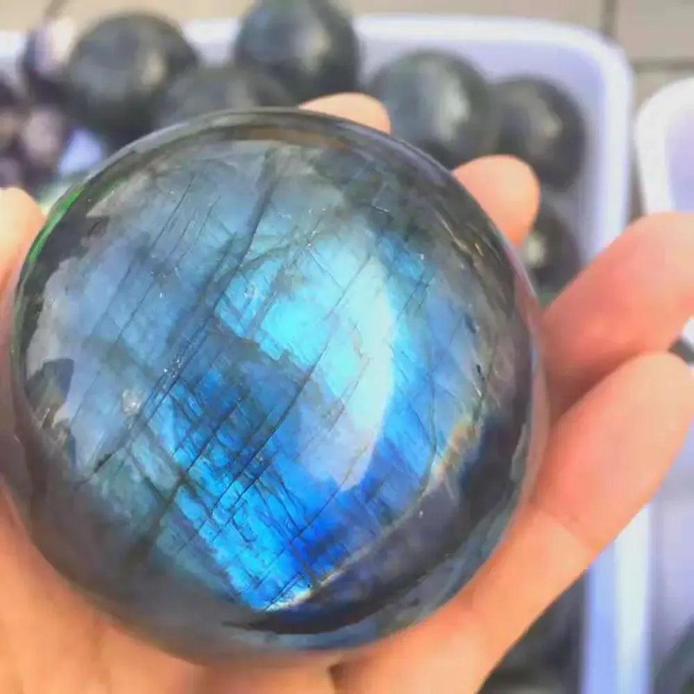 Polished Labradorite sphere, held in a hand, showcasing brilliant blue, green, and gold iridescent flash from Crystal Destiny.