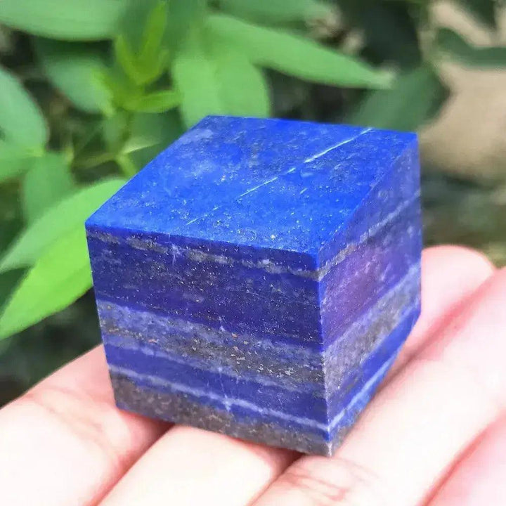 Vibrant blue Lapis Lazuli crystal cube paperweight, showcasing natural grey and white layers, held in a hand. Crystal Destiny.