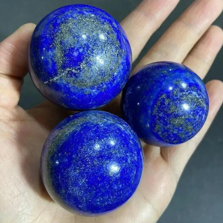 Three polished Lapis Lazuli Crystal Spheres, deep celestial blue with golden pyrite flecks, held in a hand.