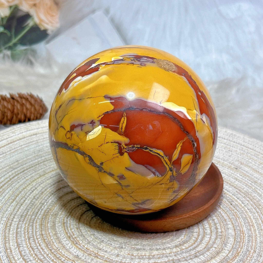 Large Mookaite sphere in red, mustard, and cream, a 2695g grounding crystal centerpiece on a wooden display stand.