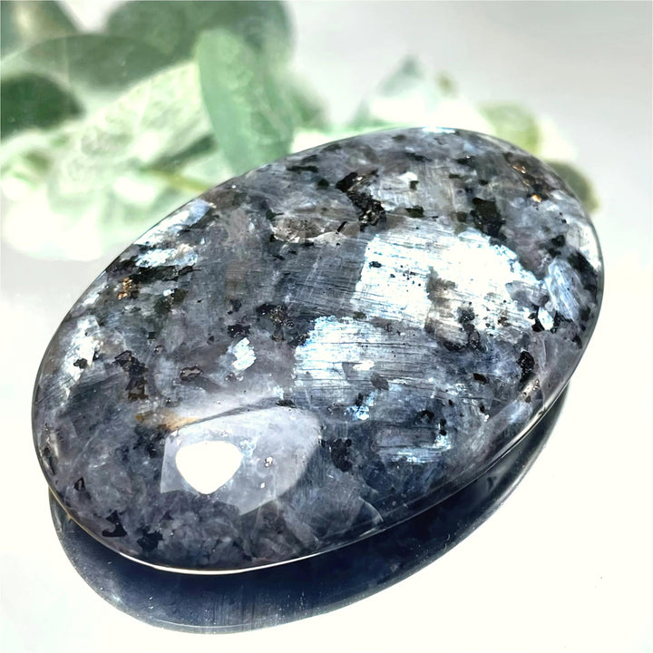 Polished Larvikite palm stone with a dark, smooth surface and shimmering silver-blue flash for grounding meditation.