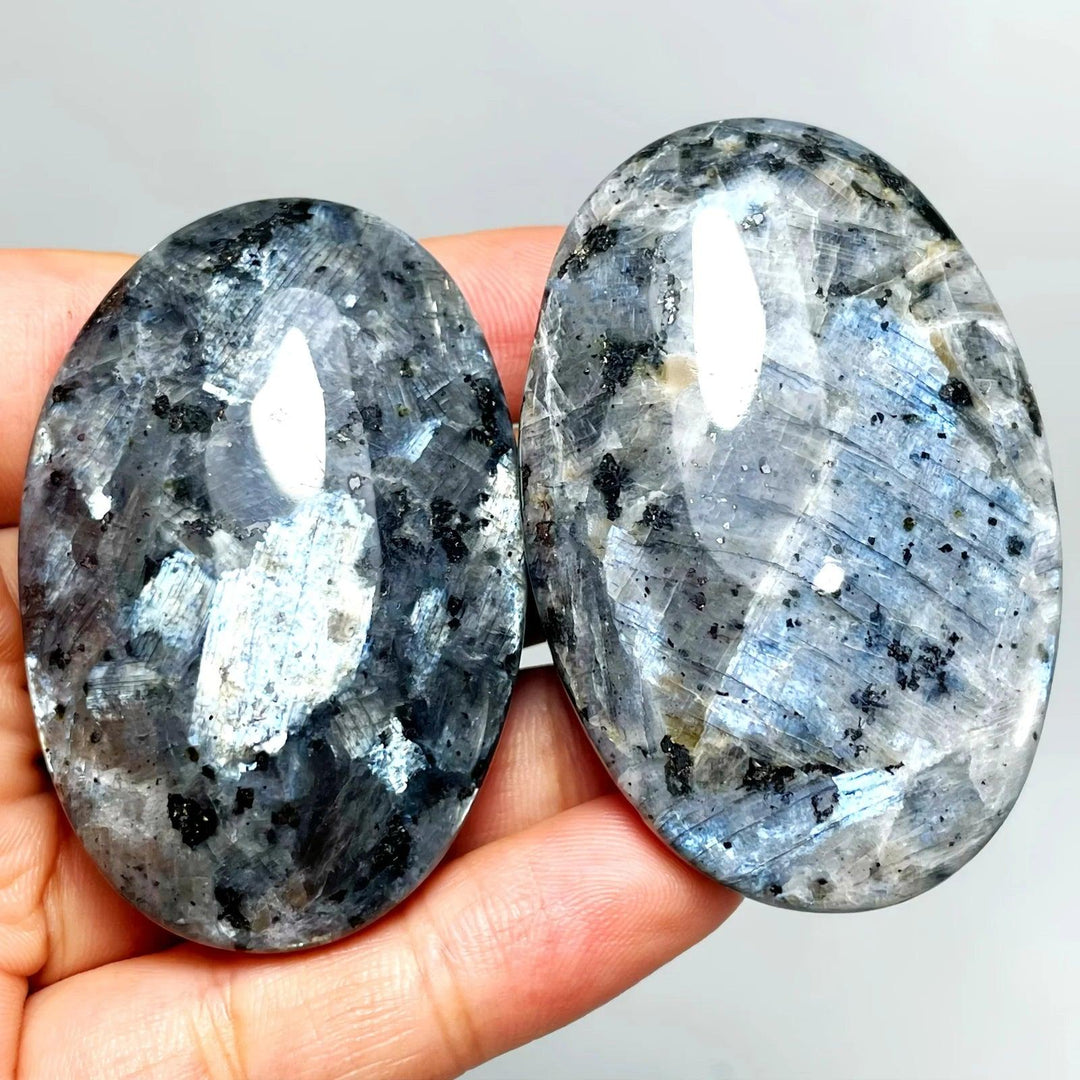Two polished Larvikite palm stones with dark grey tones and shimmering silver-blue flashes for grounding and focus.