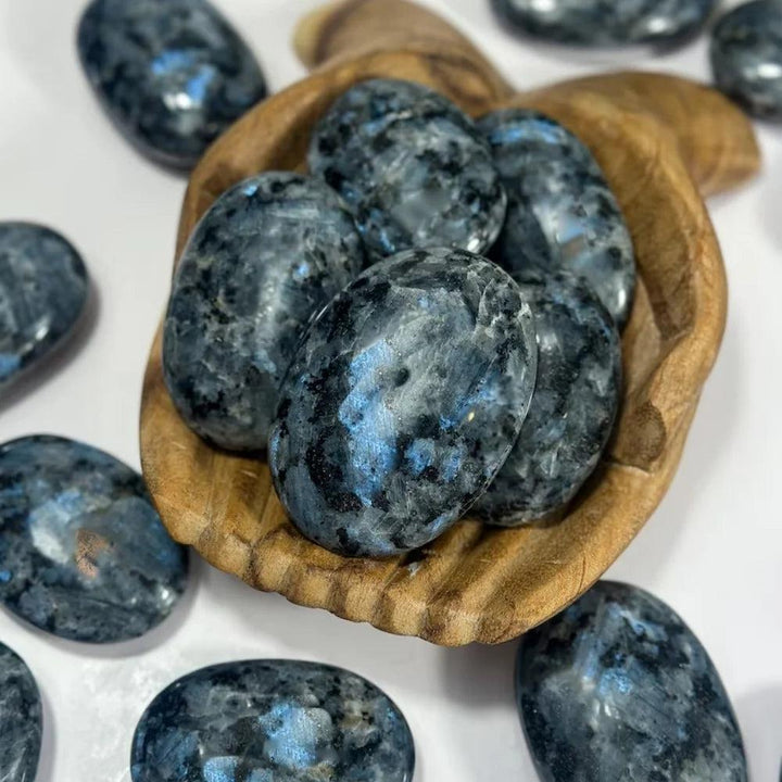 Polished blue and grey Larvikite palm stones with healing energy in a wooden bowl.
