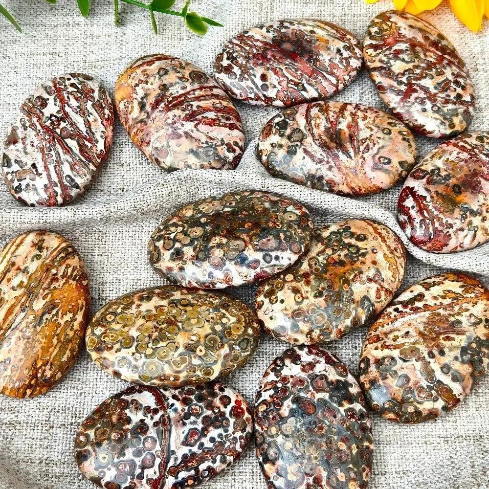 Leopard Skin Jasper Palm Stone: Polished, ergonomic stones with spotted patterns in red, black, gold, and pink.