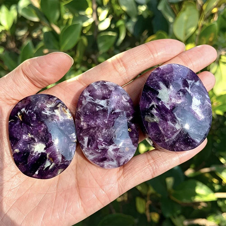 Polished violet-purple lepidolite palm stones with healing energy held in a hand.