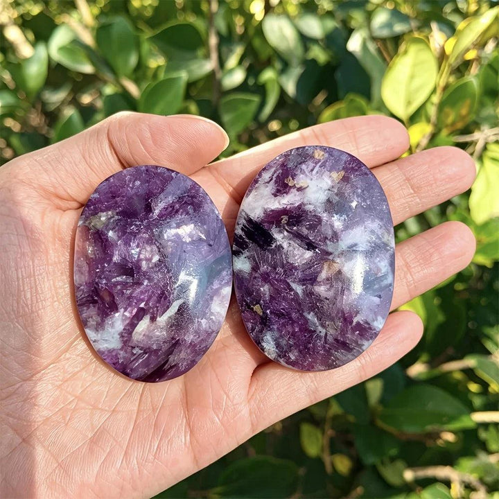 Polished violet-purple lepidolite palm stones with healing energy, held in hand.