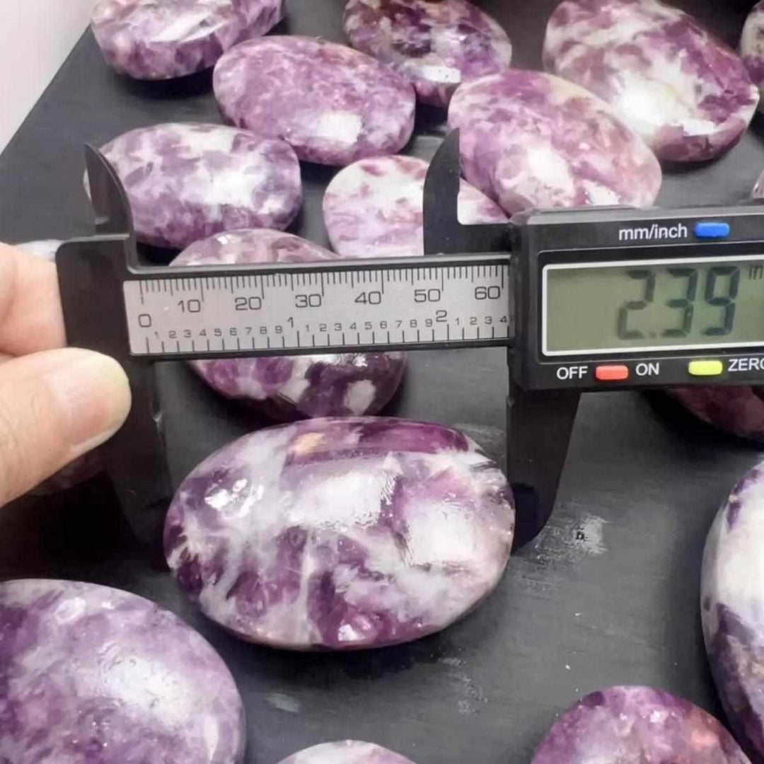 Smooth lavender lepidolite palm stone with shimmering mica, being measured for size to ensure perfect calming balance.