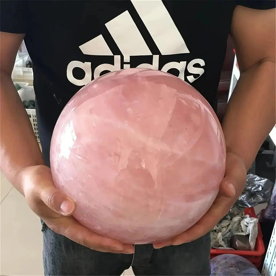 Large, polished rose quartz crystal sphere held by hands, showcasing its soft pink color and gentle energy.