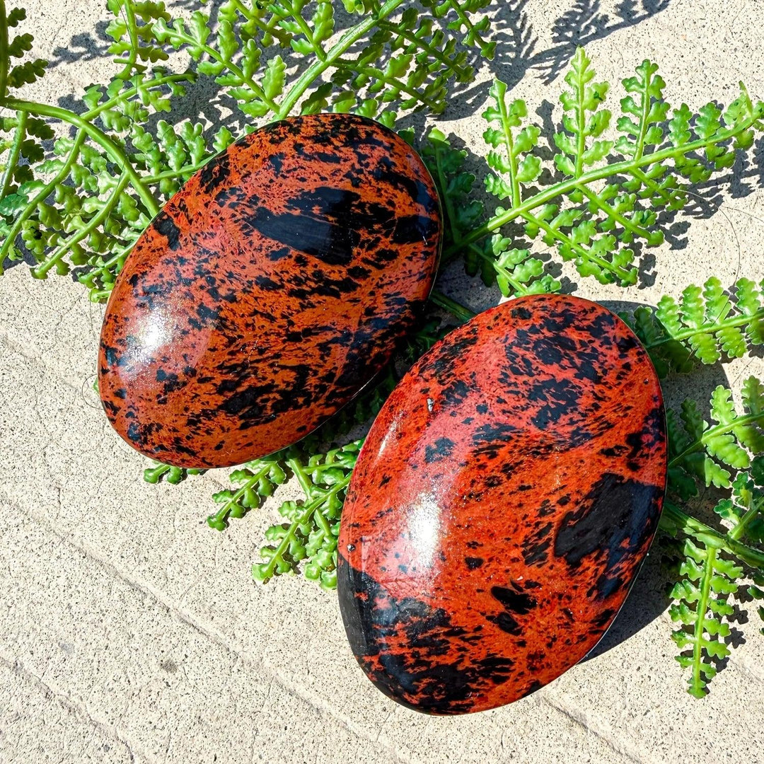 Polished mahogany obsidian palm stone with striking red-brown and black veining, perfect for healing and home decor.