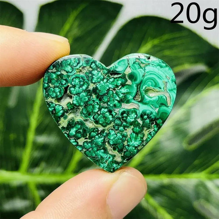 Malachite Crystal Heart: Polished deep forest green heart with mesmerizing banded patterns, held against a leaf.