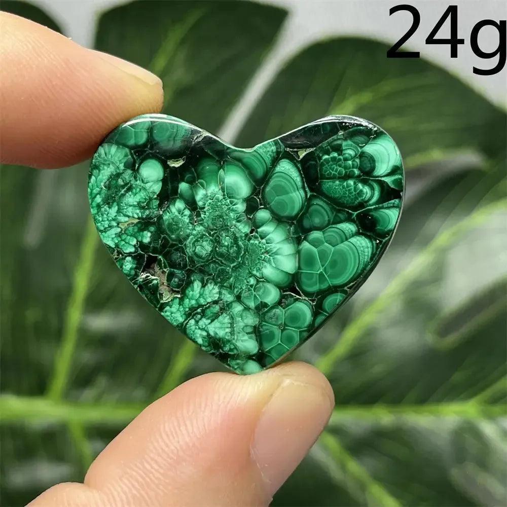 Malachite Crystal Heart: Polished deep forest green heart-shaped stone with mesmerizing banded patterns, held between fingers.