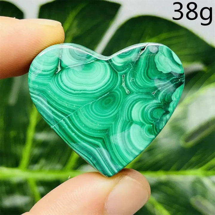 Malachite Crystal Heart: Polished deep forest green heart-shaped stone with mesmerizing swirling bands, held between fingers.