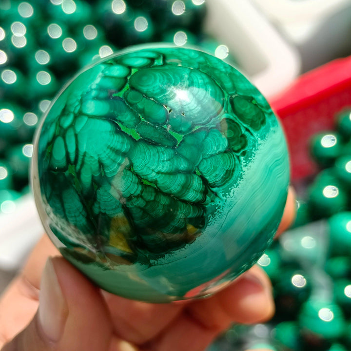 Hand-polished Malachite Crystal Sphere featuring vibrant, swirling forest green bands for heart chakra healing.