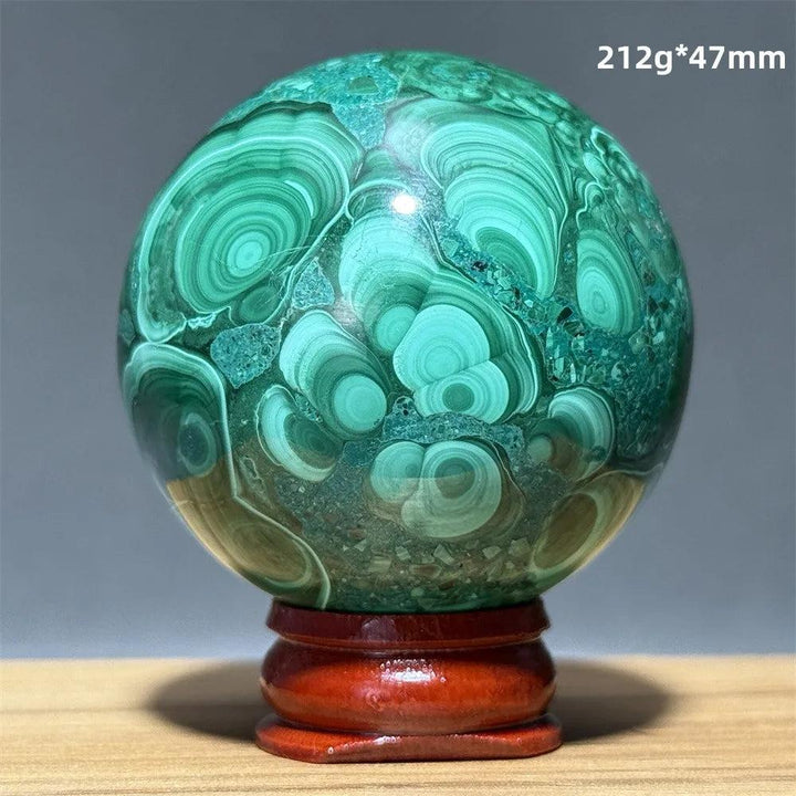 Polished Malachite crystal sphere with vibrant green banded patterns on a wooden display base for heart chakra healing.