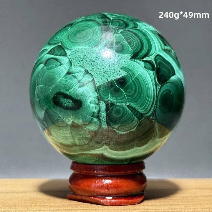 Polished 49mm malachite crystal sphere featuring vibrant emerald green banded patterns on a wooden display base.