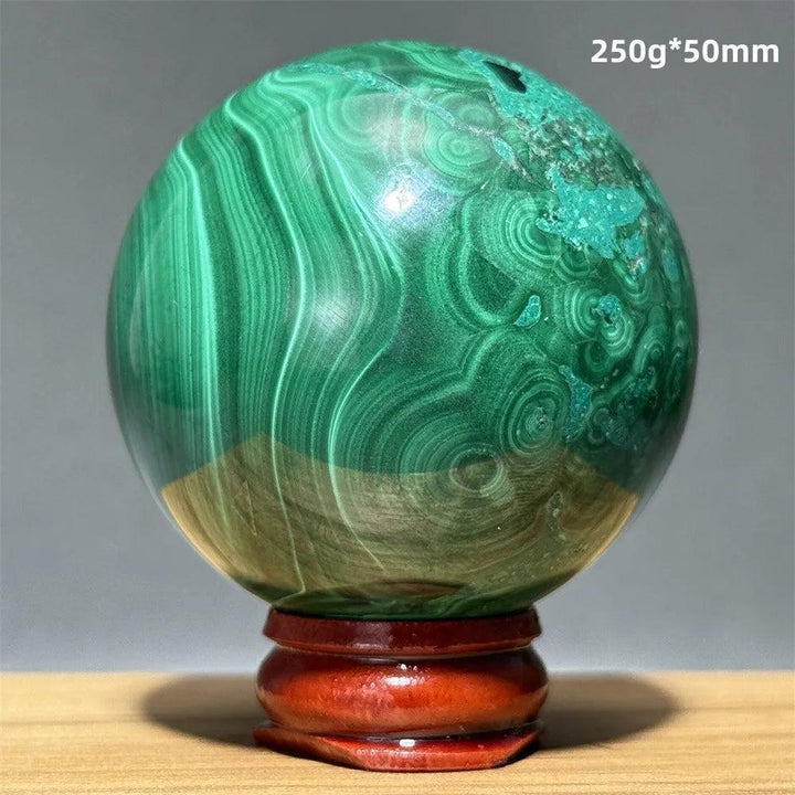 Polished 50mm malachite crystal sphere featuring vibrant green banded patterns on a wooden display base for healing.
