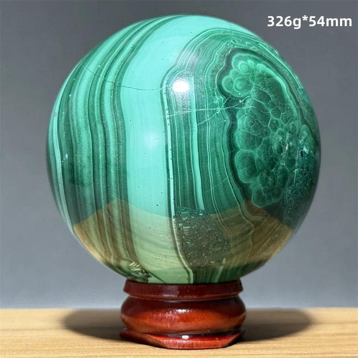 Polished 54mm Malachite crystal sphere featuring vibrant green banded patterns on a wooden display base for healing.