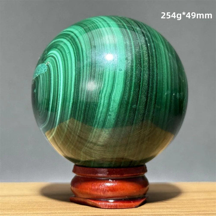 Polished malachite crystal sphere featuring vibrant green banded patterns on a wooden display base for heart healing.