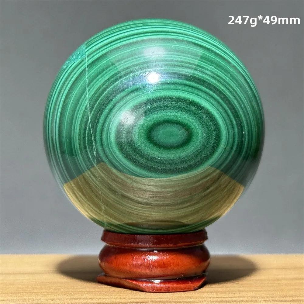 Polished malachite crystal sphere featuring vibrant green banded patterns on a wooden display base for heart healing.