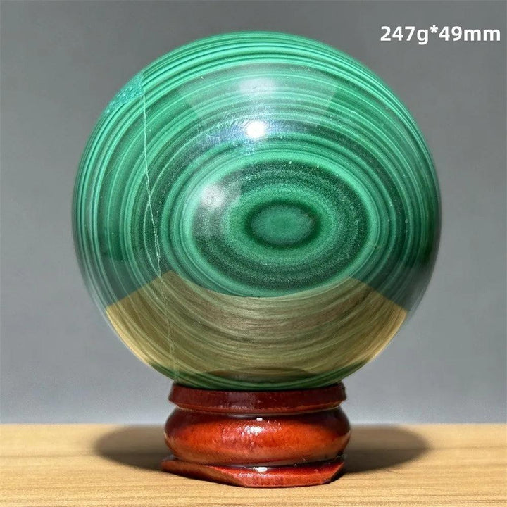 Polished malachite crystal sphere featuring vibrant green banded patterns on a wooden display base for heart healing.