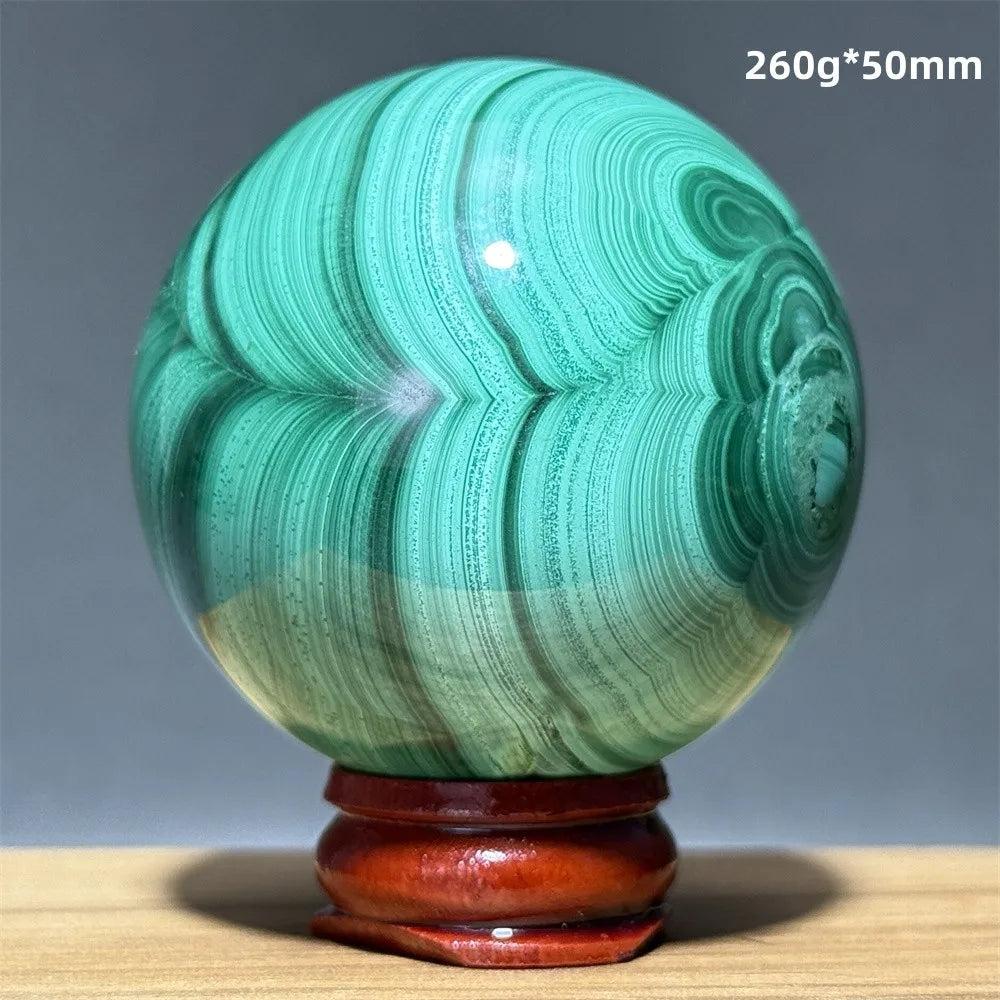 Polished 50mm Malachite crystal sphere featuring vibrant emerald green banded patterns on a wooden display base.