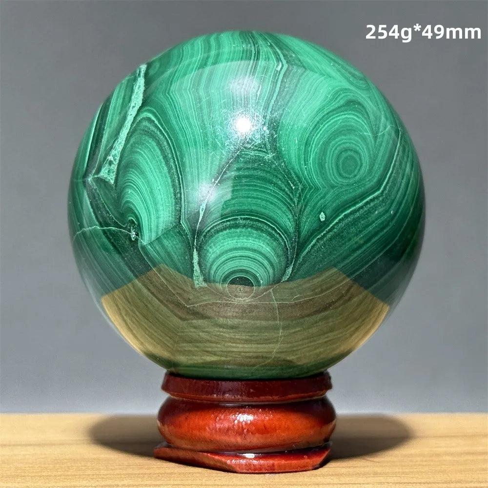 Polished malachite crystal sphere featuring vibrant green banded patterns on a wooden display base for transformation.
