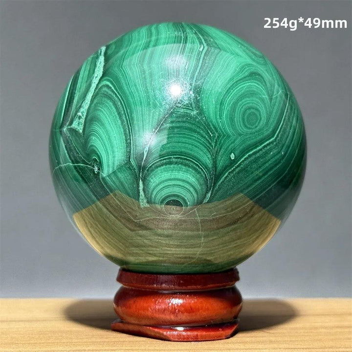 Polished malachite crystal sphere featuring vibrant green banded patterns on a wooden display base for transformation.