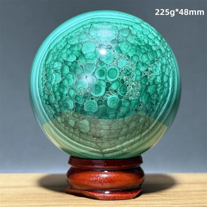 Polished malachite crystal sphere featuring vivid green banded patterns on a wooden display base for heart chakra healing.