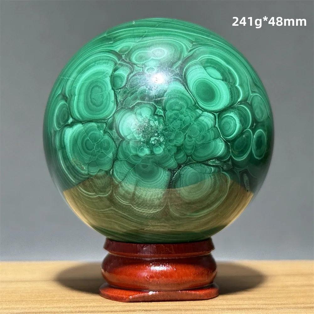 Polished malachite crystal sphere with vivid green banded patterns on a wooden display base for heart chakra healing.