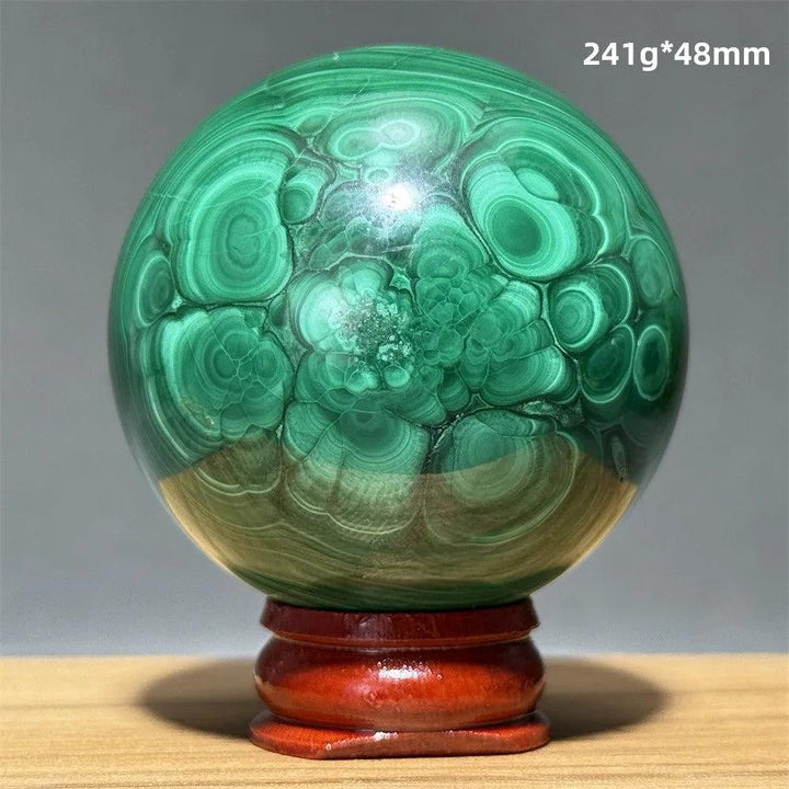 Polished malachite crystal sphere with vivid green banded patterns on a wooden display base for heart chakra healing.