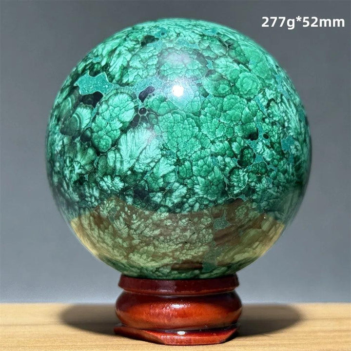 Polished malachite crystal sphere with vivid emerald green banding on a wooden display base for heart chakra healing.