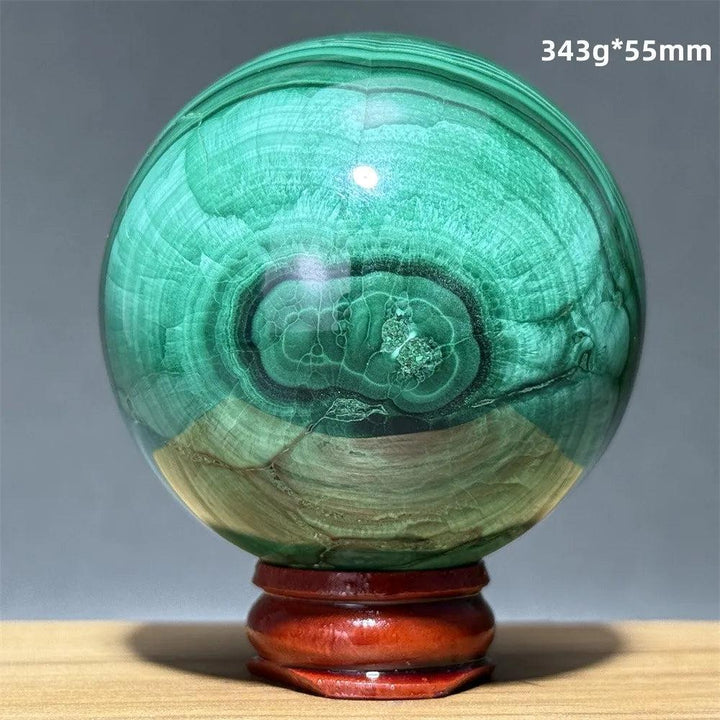 Hand-polished malachite crystal sphere with vibrant green banded patterns on a wooden display base for heart healing.