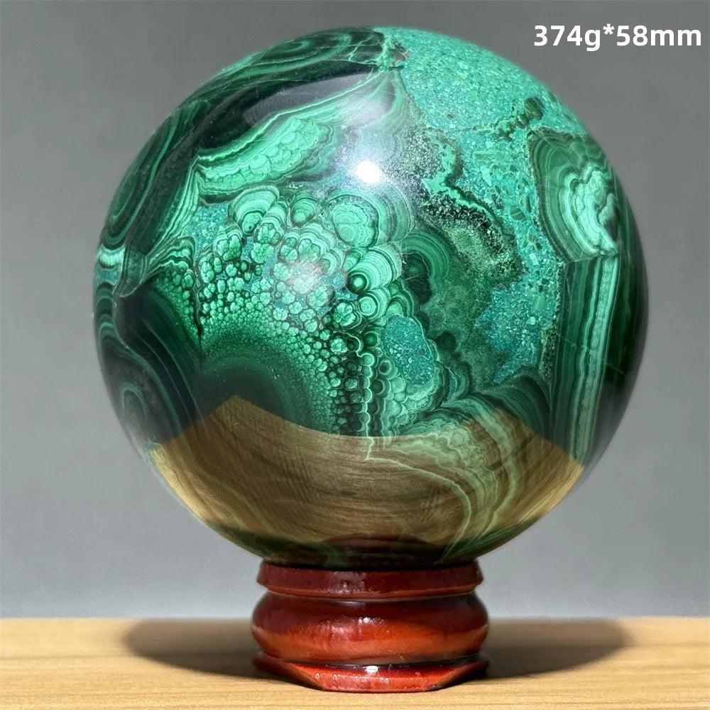 Polished malachite crystal sphere featuring vibrant green banded patterns on a wooden display base for heart healing.