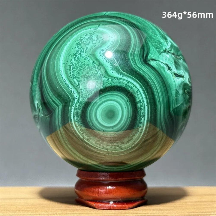 Polished malachite crystal sphere featuring vibrant green banded patterns on a wooden display base for transformation.