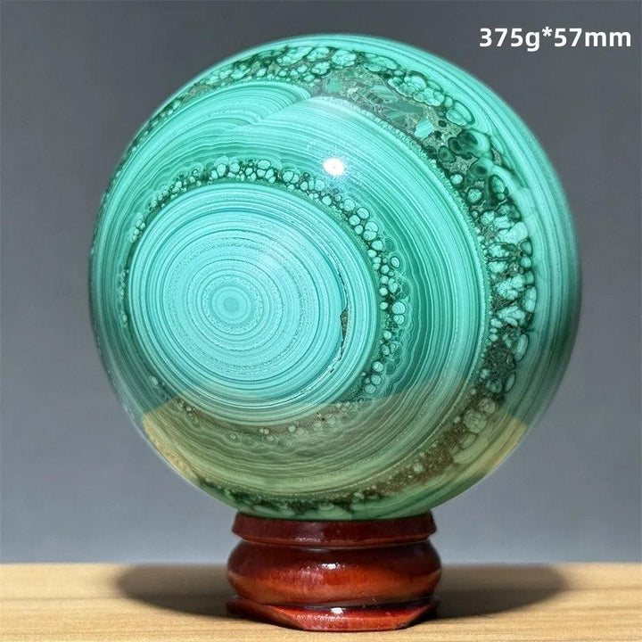 Polished 57mm malachite crystal sphere featuring vibrant emerald green banded patterns on a wooden display base.