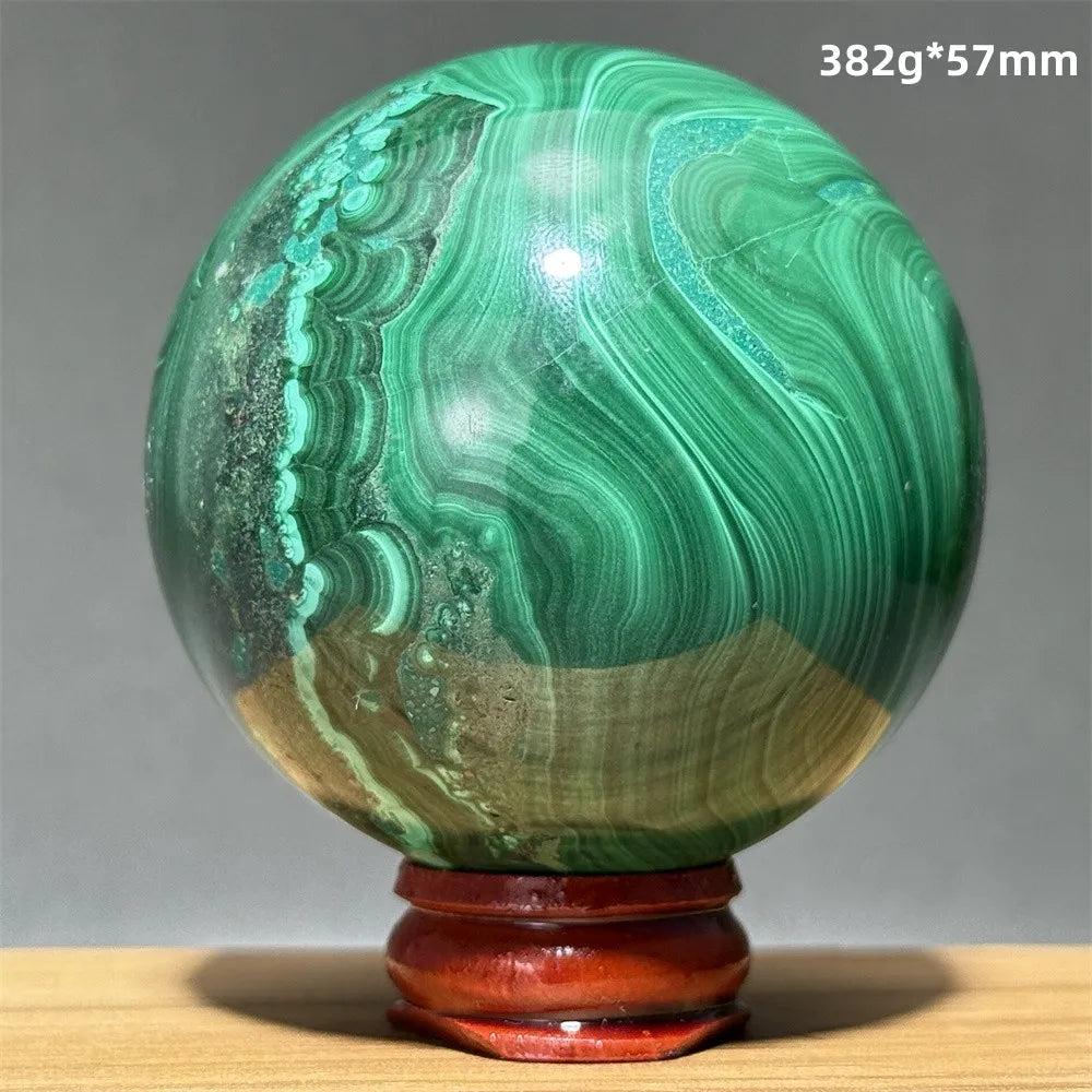 Polished malachite crystal sphere featuring vibrant green banded patterns on a wooden display base for healing energy.