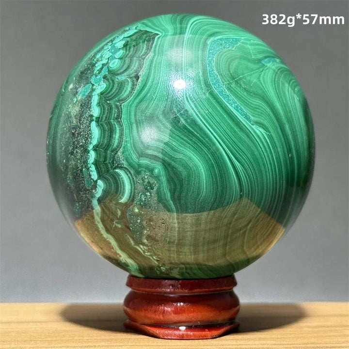 Polished malachite crystal sphere featuring vibrant green banded patterns on a wooden display base for healing energy.