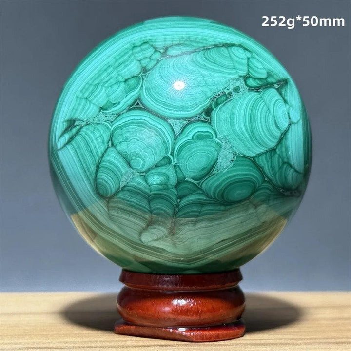 Polished Malachite crystal sphere featuring vibrant green banded patterns on a wooden display base for heart healing.