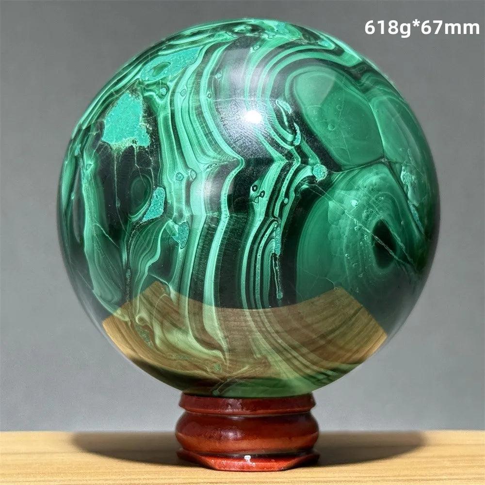 Polished malachite crystal sphere featuring vibrant green banded patterns on a wooden display base for transformation.