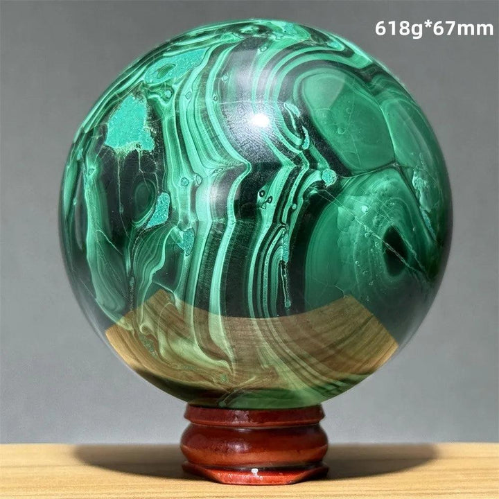 Polished malachite crystal sphere featuring vibrant green banded patterns on a wooden display base for transformation.