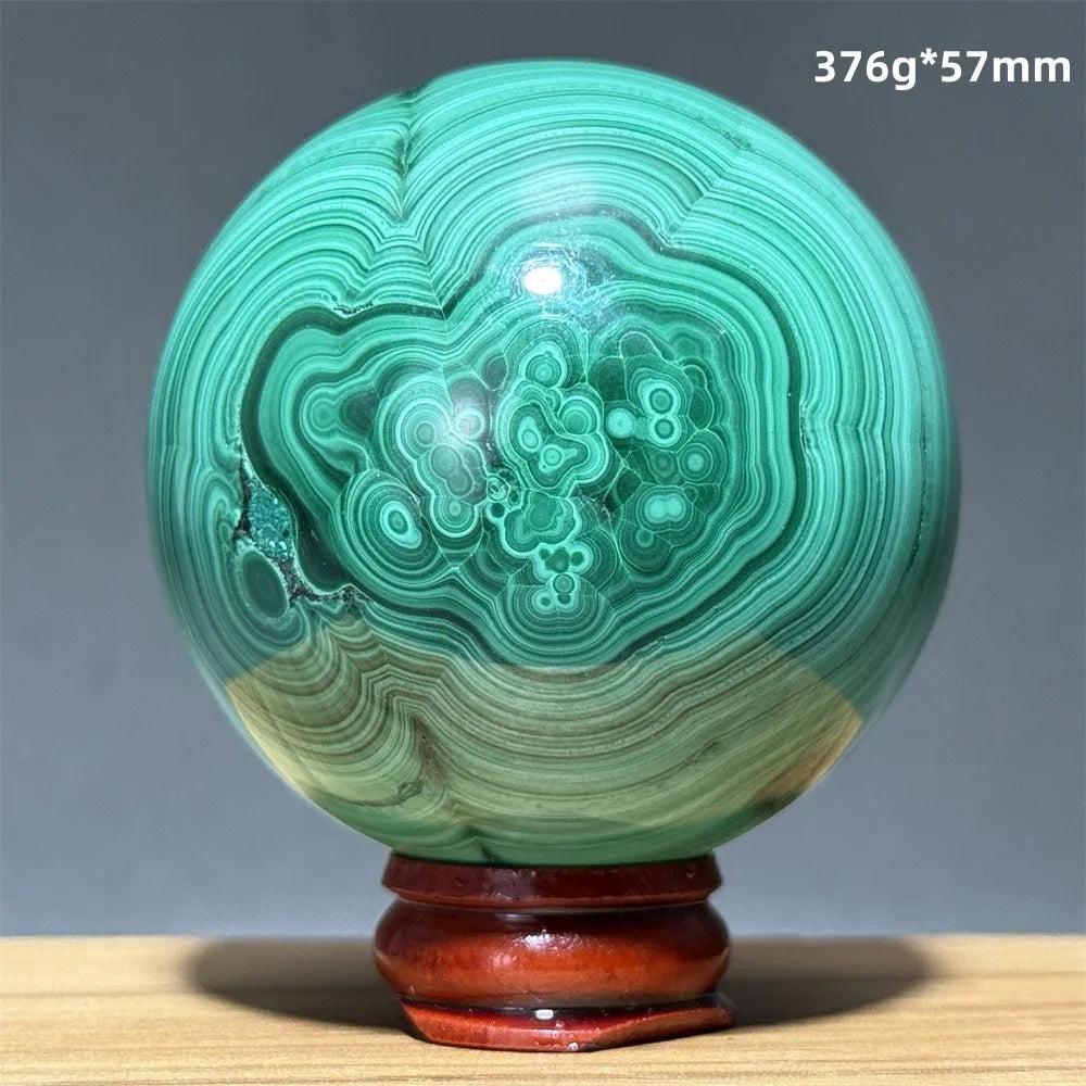 Polished Malachite crystal sphere featuring vibrant green banded patterns on a wooden display base for heart healing.