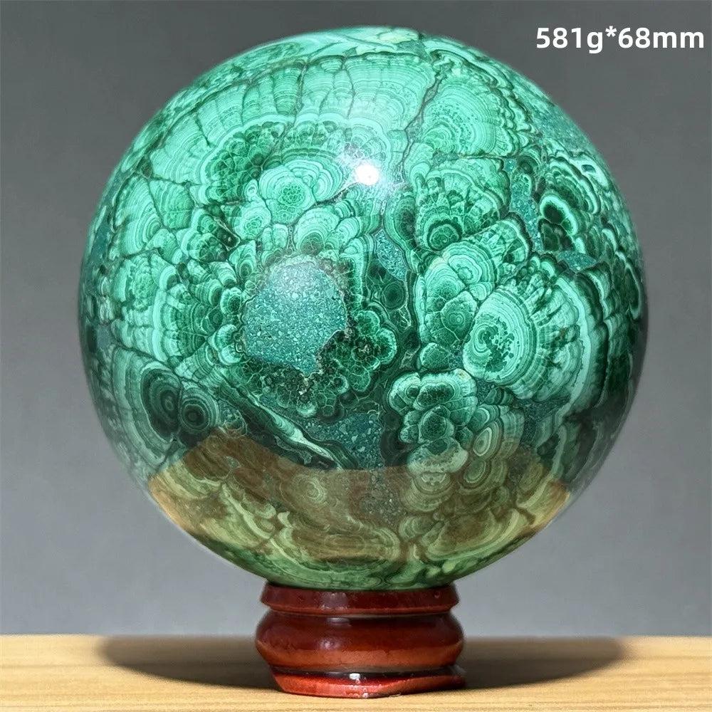 Polished Malachite crystal sphere featuring vibrant green banded patterns on a wooden display base for transformation.