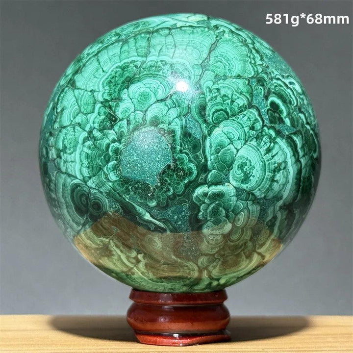 Polished Malachite crystal sphere featuring vibrant green banded patterns on a wooden display base for transformation.