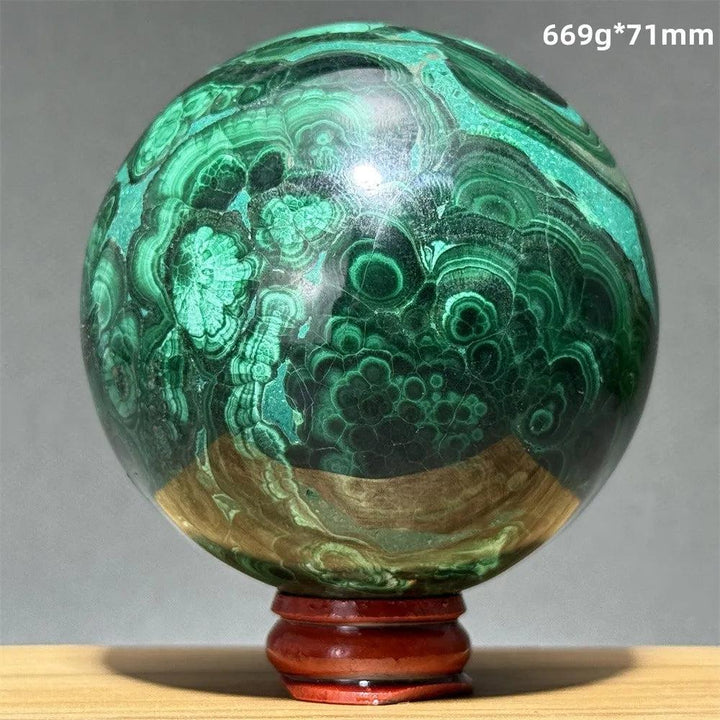 Polished 71mm malachite crystal sphere featuring vibrant green banded patterns on a wooden display base for healing.