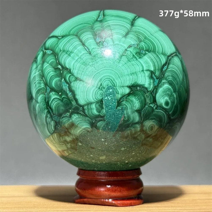Polished 58mm malachite crystal sphere featuring vibrant green banded patterns on a wooden display base for healing.