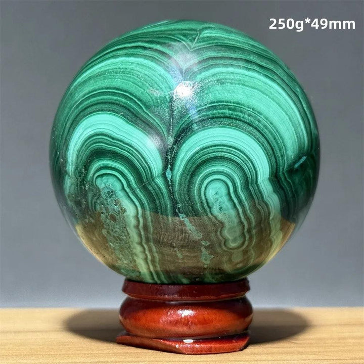 Polished 49mm Malachite crystal sphere featuring vibrant green banded patterns on a wooden display base for healing.