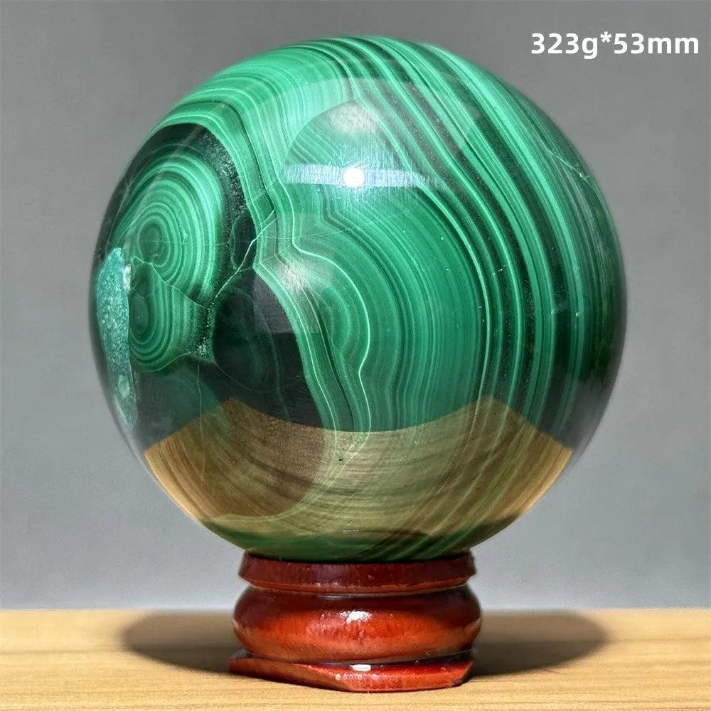 Polished malachite crystal sphere featuring vibrant green banded patterns on a wooden display base for heart healing.