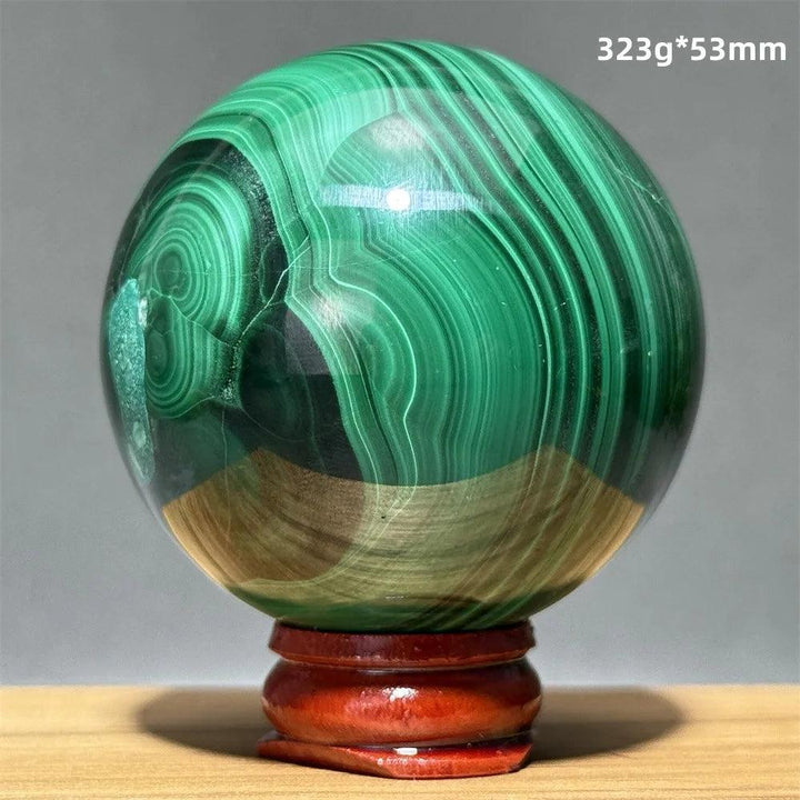 Polished malachite crystal sphere featuring vibrant green banded patterns on a wooden display base for heart healing.