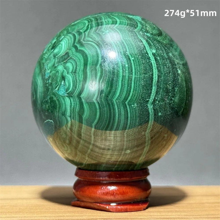 Polished malachite crystal sphere with vibrant green banded patterns on a wooden display base for heart chakra healing.