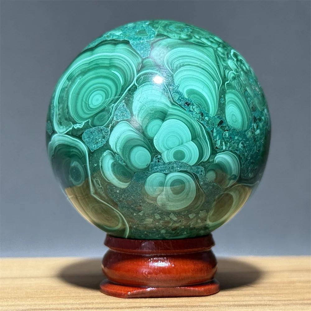Polished Malachite crystal sphere featuring vibrant green banded patterns on a wooden display base for transformation.